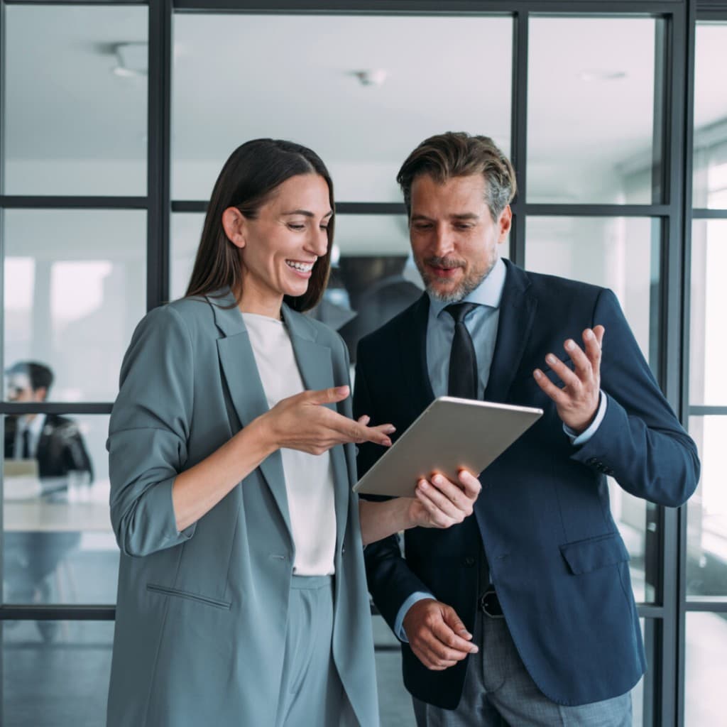 Two colleagues reviewing work on a tablet in a bright contemporary office—precise, collegial partnership.